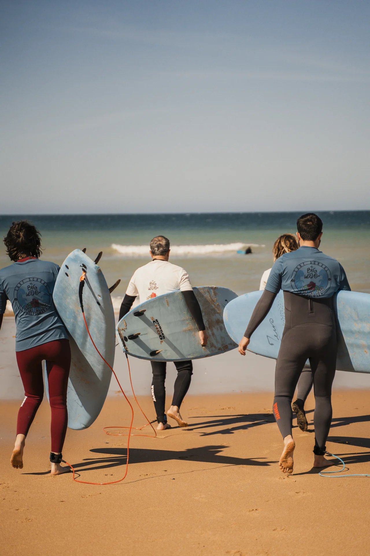 Alumnos reales de Big Wave caminando hacia el mar con sus tablas