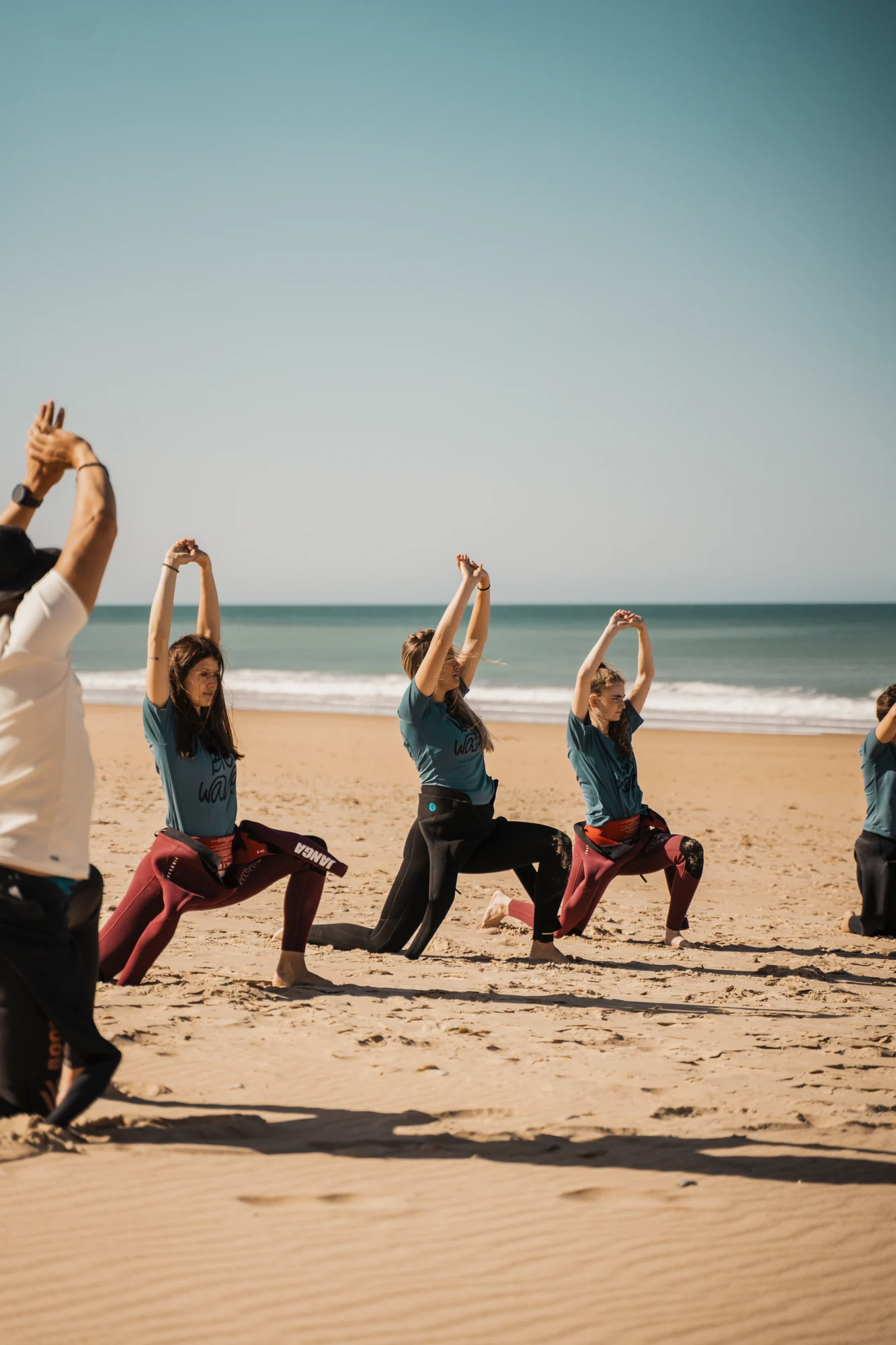 Grupo de adultos calentando en la playa antes de su clase de surf